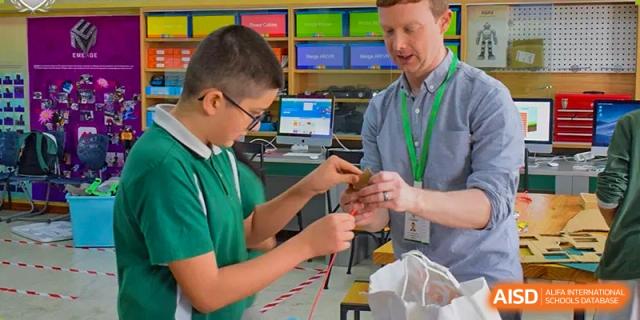 A teacher assisting a student with a hands-on construction or engineering project in a workshop or classroom at Britannia International School Guangzhou.