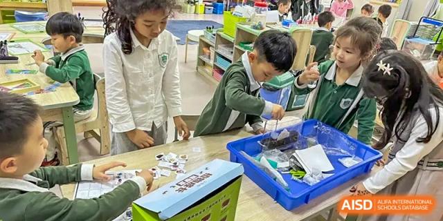A student in a green shirt working on a robotics or construction project, handling small parts on the floor, at Britannia International School Guangzhou.