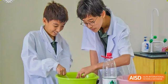 Two students in lab coats conducting a hands-on science experiment, mixing ingredients in a green bowl, at Britannia International School Guangzhou.