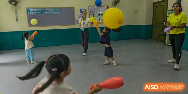 Children playing with large yellow and blue balloons and a red cone-shaped object in an indoor area at Britannia International School Guangzhou.