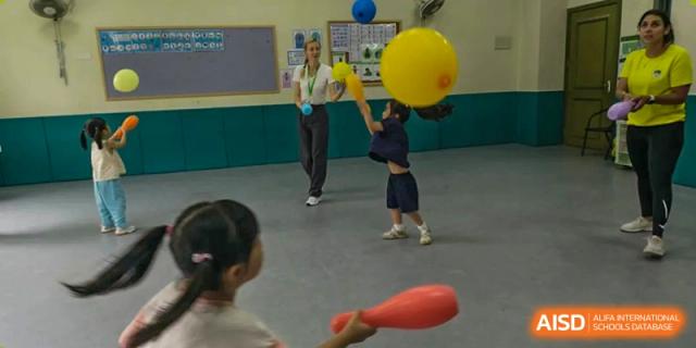 Children playing with large yellow and blue balloons and a red cone-shaped object in an indoor area at Britannia International School Guangzhou.