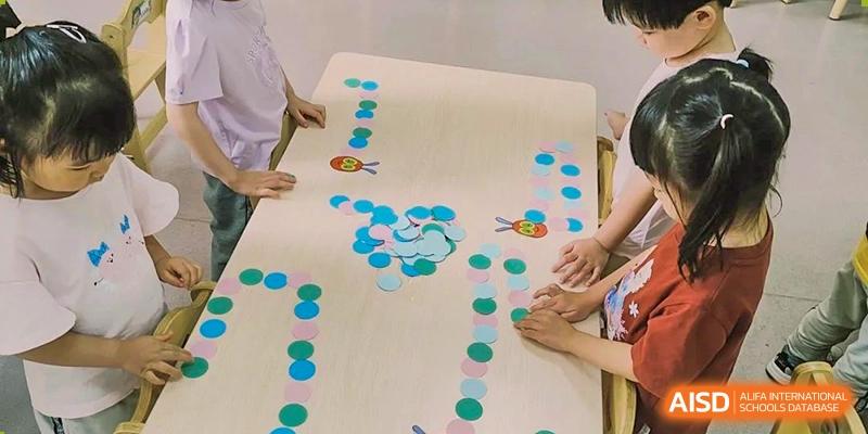 Several people gathered around a large wooden table with small colorful paper circles arranged in paths and designs, engaged in a table activity at Britannia International School Guangzhou.