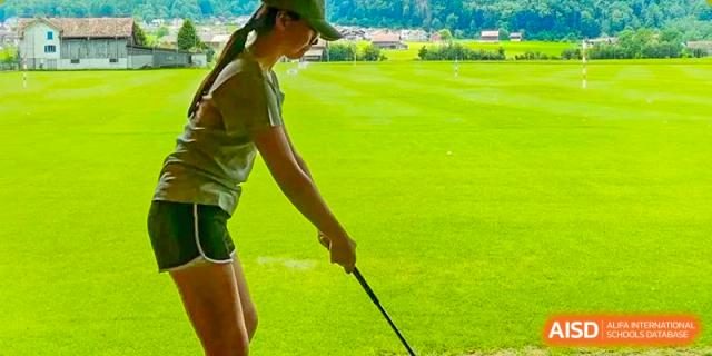 A young person outdoors practicing a golf swing on a bright green course, with a grassy field and trees in the background, at Britannia International School Guangzhou.