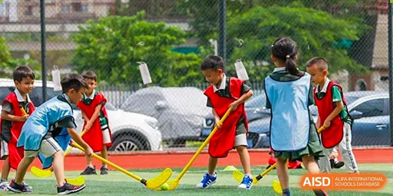 A student in a red vest practicing field hockey outdoors, holding a yellow hockey stick, at Britannia International School Guangzhou.