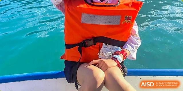 Close-up of a person wearing an orange life vest and shorts while sitting on a boat or near water at Britannia International School Guangzhou.