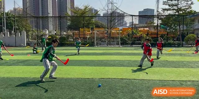 Children playing field hockey with sticks and a blue ball on an artificial turf sports pitch at Britannia International School Guangzhou.