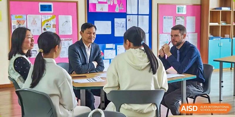 A male teacher in a suit interviewing a female student who is sitting with her back to the camera, in a formal setting at Britannia International School Guangzhou.