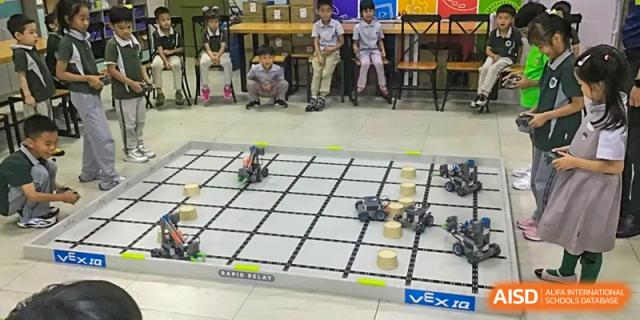 Students watching small VEX robots on a grid field during a robotics competition or activity at Britannia International School Guangzhou.