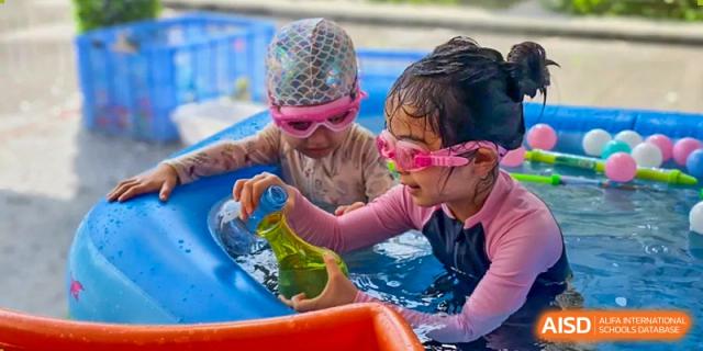 Two children wearing swim caps and goggles playing with a yellow water bottle in a small inflatable pool at Britannia International School Guangzhou.