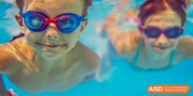 Close-up of a child wearing blue and red swimming goggles with their face partially submerged in a pool at Britannia International School Guangzhou.