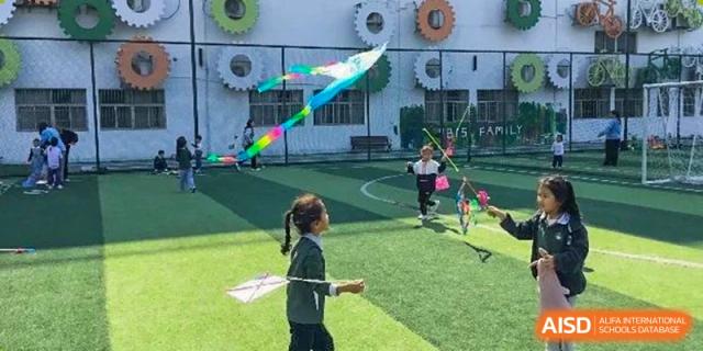 A student outdoors on a green field making large bubbles with bubble wands, with other children and school buildings in the background at Britannia International School Guangzhou.
