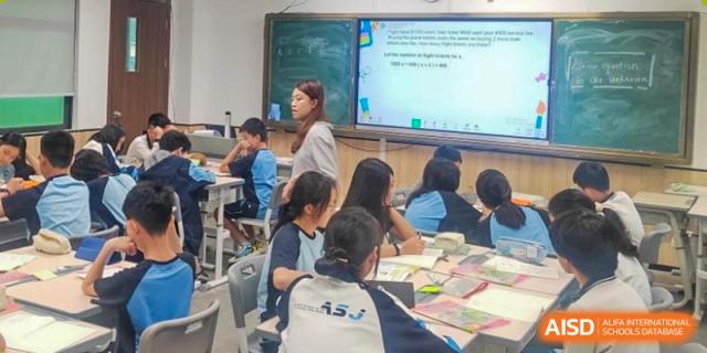 A teacher instructing students in a busy classroom, writing on the traditional blackboard above the smart screen at the Affiliated School of JNU for Hong Kong & Macao Students.
