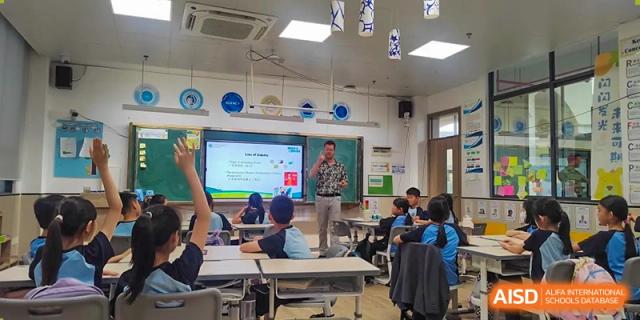 A teacher presenting a lesson using a projector screen to students in a modern classroom at the Affiliated School of JNU for Hong Kong & Macao Students.