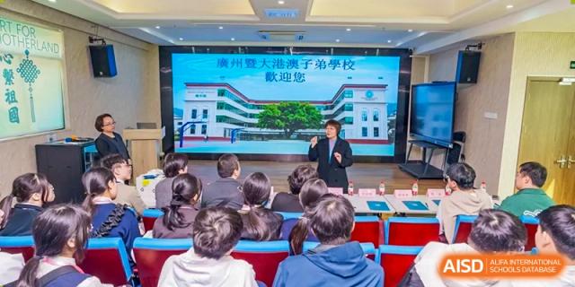 An adult giving a presentation on a large screen to a group of students in an auditorium at the Affiliated School of JNU for Hong Kong & Macao Students.