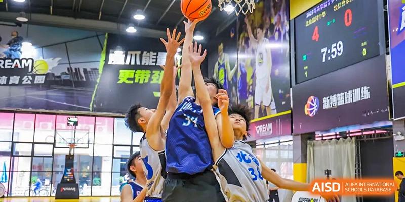 Intense action shot of students from the Affiliated School of JNU for Hong Kong & Macao Students jumping and competing for a rebound or block during a basketball game.