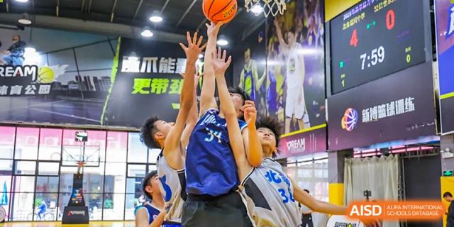 Intense action shot of students from the Affiliated School of JNU for Hong Kong & Macao Students jumping and competing for a rebound or block during a basketball game.