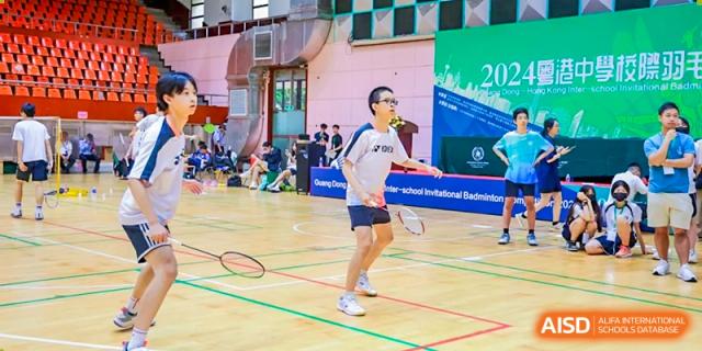 A student from the Affiliated School of JNU for Hong Kong & Macao Students wearing glasses serving or hitting a shot on a badminton court during a game.