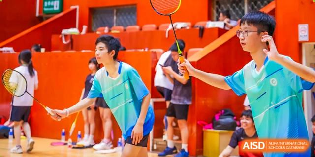 A student from the Affiliated School of JNU for Hong Kong & Macao Students in a blue shirt preparing to hit a shuttlecock during a badminton match.