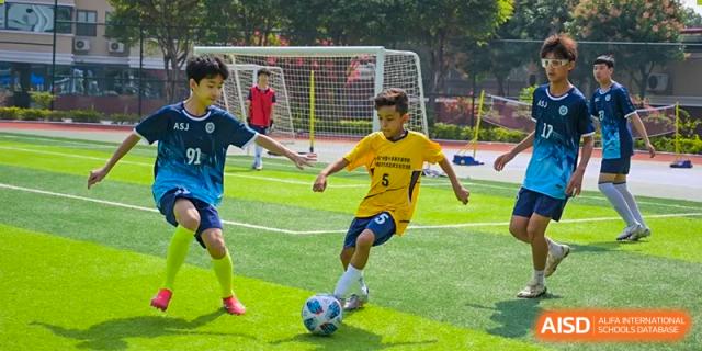 A student in a yellow jersey from the Affiliated School of JNU for Hong Kong & Macao Students dribbling a soccer ball near the goal during practice or a match.