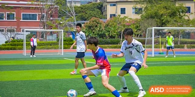 Students from the Affiliated School of JNU for Hong Kong & Macao Students competing fiercely for the ball during a soccer match on an outdoor field.