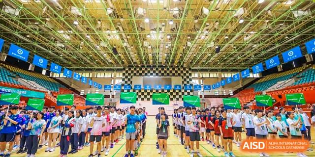 A large group of students from the Affiliated School of JNU for Hong Kong & Macao Students gathered in an indoor gymnasium for an assembly or sports event.