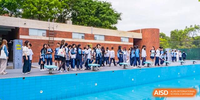 A group of students from the Affiliated School of JNU for Hong Kong & Macao Students standing near the edge of an outdoor swimming pool during an activity or class.