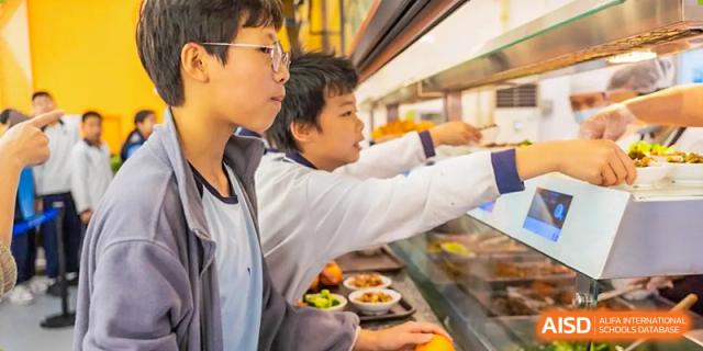 Students from the Affiliated School of JNU for Hong Kong & Macao Students selecting food at a cafeteria or serving line.