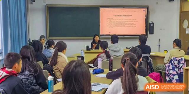 Students seated in a classroom listening attentively to an adult or teacher giving a presentation or lecture projected onto a screen at Beijing Academy International Department (BAID).
