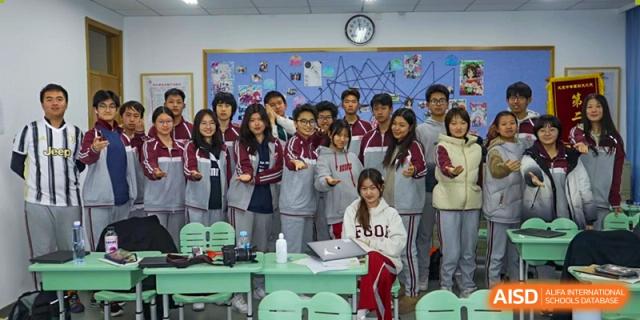 A classroom full of students, many holding awards or certificates, smiling for a group photo to celebrate their achievements at Beijing Academy International Department (BAID).