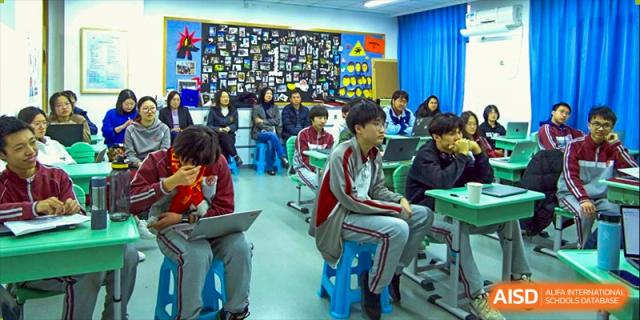 Students working with laptops in a brightly colored classroom with a large display on the wall at Beijing Academy International Department (BAID).