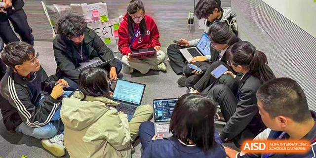 Students sitting on the floor, collaborating intently on their laptops during a flexible learning session at Beijing Academy International Department (BAID).