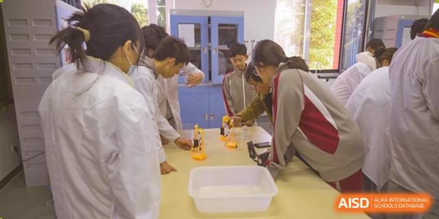 Students in lab coats working together on a practical science experiment using glassware and a burner at Beijing Academy International Department (BAID).