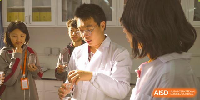 A student in a white lab coat holds up a clear vial, engaging in a science experiment with a classmate at Beijing Academy International Department (BAID).
