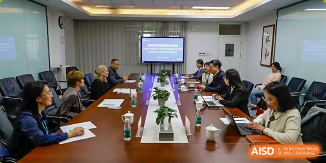 A formal staff or board meeting taking place around a long table with a presentation projected onto a screen at Beijing Academy International Department (BAID).