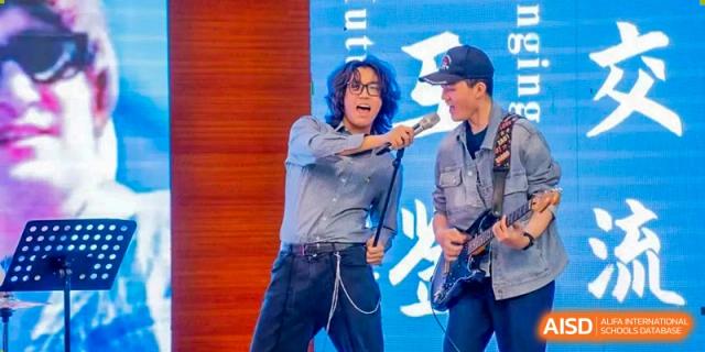 Two students performing an energetic rock or pop song on stage with microphones and a guitar at Beijing Academy International Department (BAID).