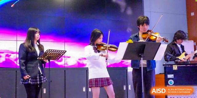 A female student in a white top and plaid skirt passionately playing the violin in a musical performance at Beijing Academy International Department (BAID).