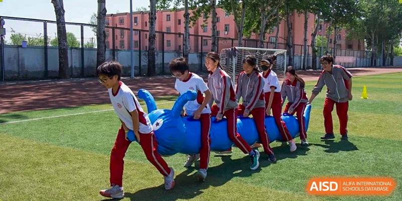Students participating in a fun, team-building relay race while holding a large blue inflatable tube on the sports field at Beijing Academy International Department (BAID).