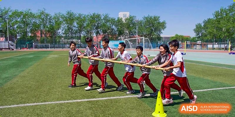 A group of students wearing red and white uniforms participating in an outdoor tug-of-war competition on the field at Beijing Academy International Department (BAID).
