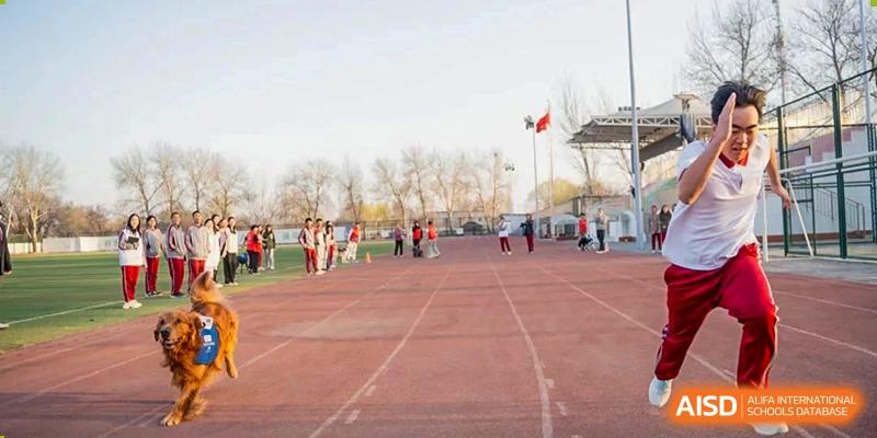Students gathered near a red running track and field, with flags flying, during an outdoor sports day at Beijing Academy International Department (BAID).