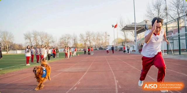 Students gathered near a red running track and field, with flags flying, during an outdoor sports day at Beijing Academy International Department (BAID).