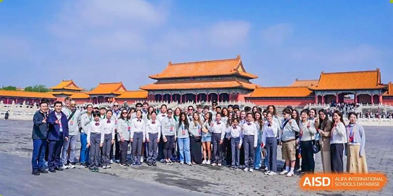 A large group of students in white shirts and dark pants posing for a group photo in front of the Forbidden City during a cultural field trip at Beijing Academy International Department (BAID).