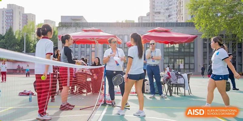 Two female students dressed in white stand on a court, playing a game of outdoor tennis at Beijing Academy International Department (BAID).