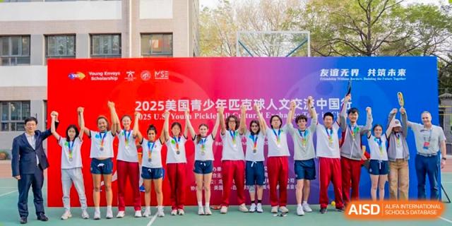 A group of students in red and white shirts celebrating a victory with their arms raised after the "2025 US Youth Pickleball Cup" competition at Beijing Academy International Department (BAID).