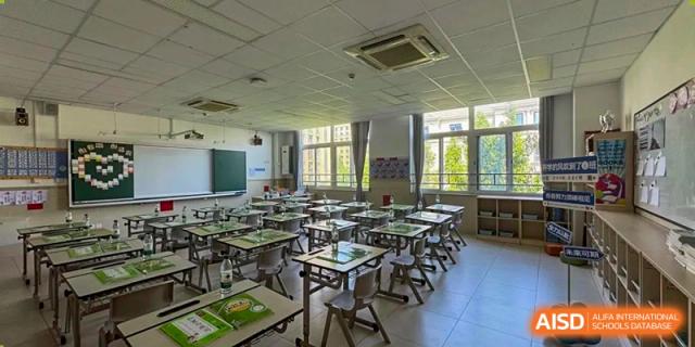 A view of an empty classroom with rows of desks and chairs neatly arranged, a whiteboard, and ceiling fans, at Beijing SMIC Private School.