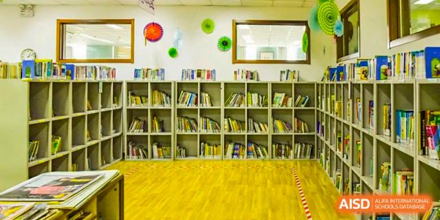 A wide shot of a library or reading area with low bookshelves, a yellow carpet, and decorative elements on the back wall, at Beijing SMIC Private School.