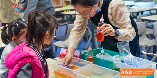 A close-up of an adult and students participating in a science experiment involving a clear liquid in a plastic container, at Beijing SMIC Private School.