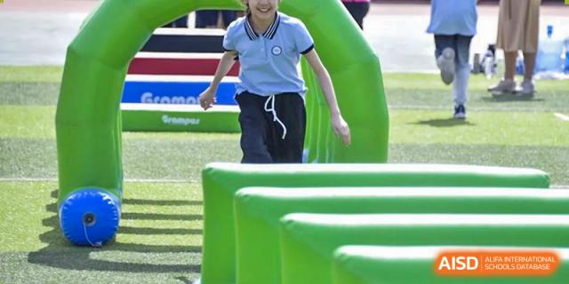A close-up shot of a student participating in an outdoor obstacle course event, stepping over large, bright green inflatable blocks, at Beijing SMIC Private School.