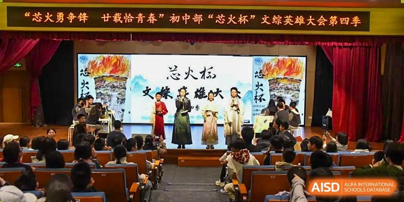 A theatrical or cultural performance with students in elaborate costumes on a stage in an auditorium, with a large backdrop featuring Chinese calligraphy, at Beijing SMIC Private School.