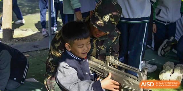 A young male student in a dark vest and white shirt handling a plastic machine gun or prop during an activity, at Beijing SMIC Private School.
