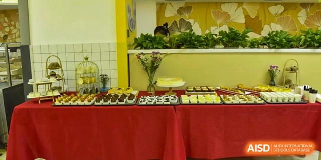 A buffet table covered with a red cloth and various healthy snacks and desserts, including fresh fruit and vegetables, at Beijing SMIC Private School.